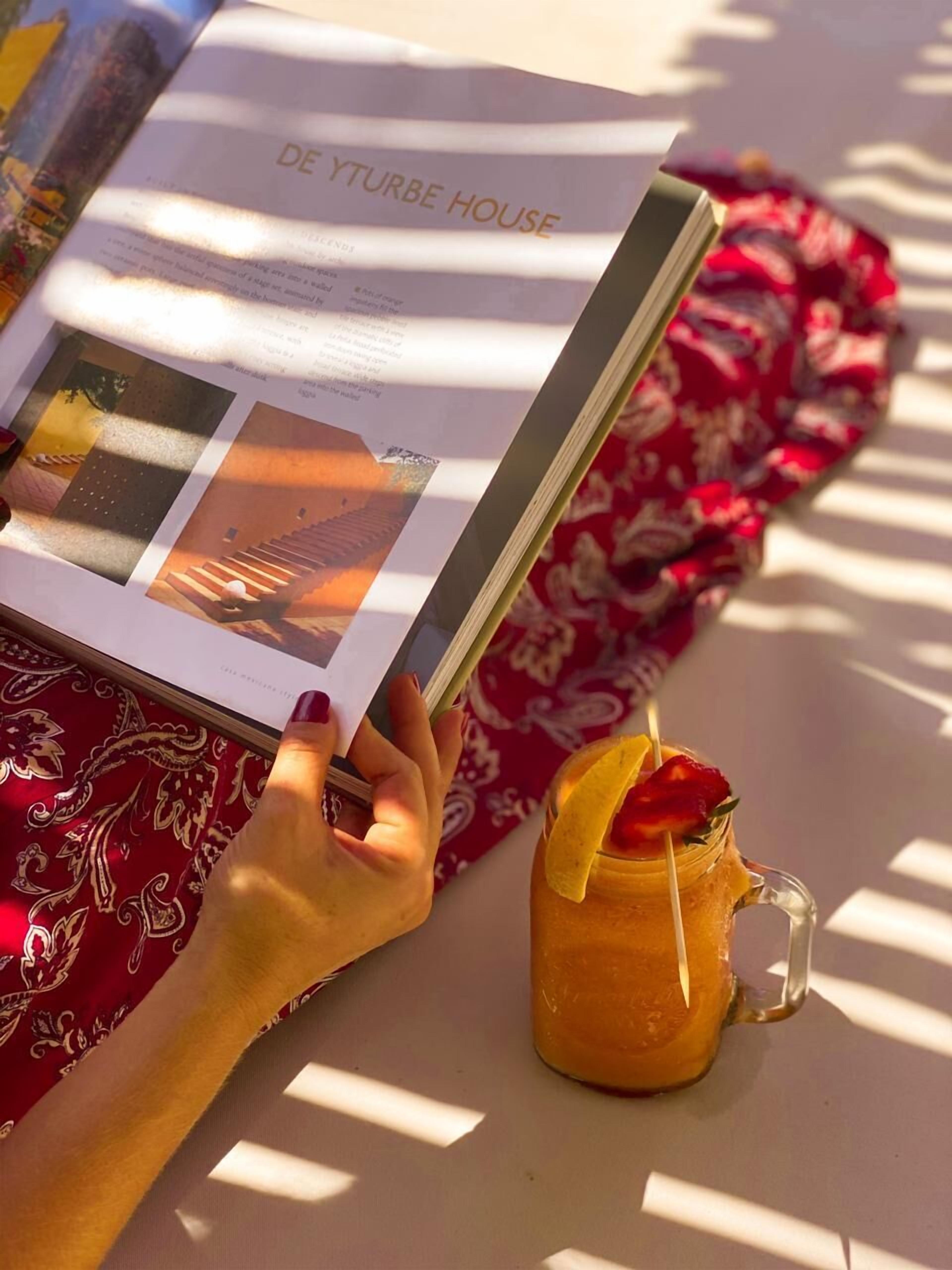 A person reading a magazine titled "DE YTURBE HOUSE" with a drink beside them.