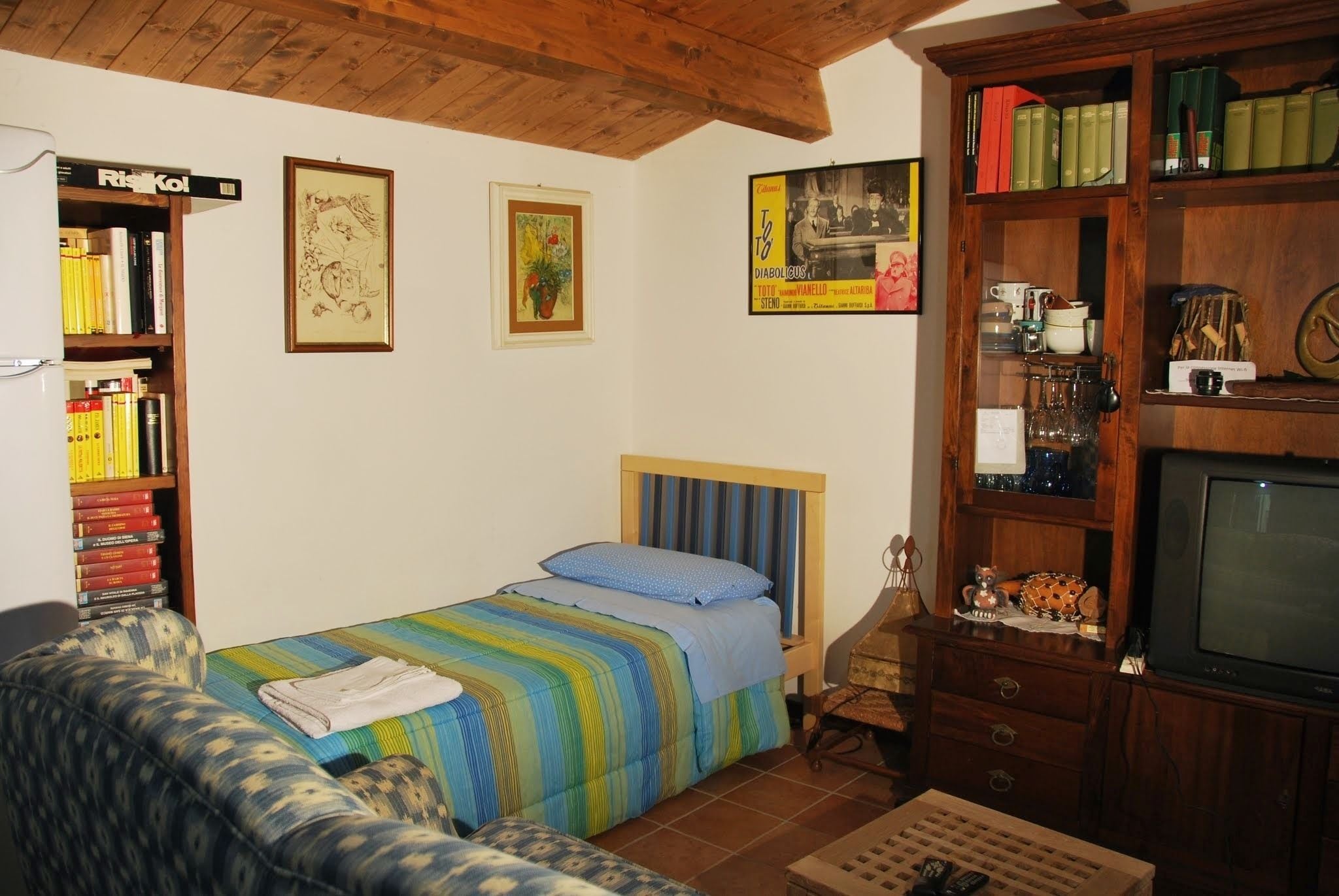 A cozy room with a bed, a chair, a wooden bookshelf, and a television.