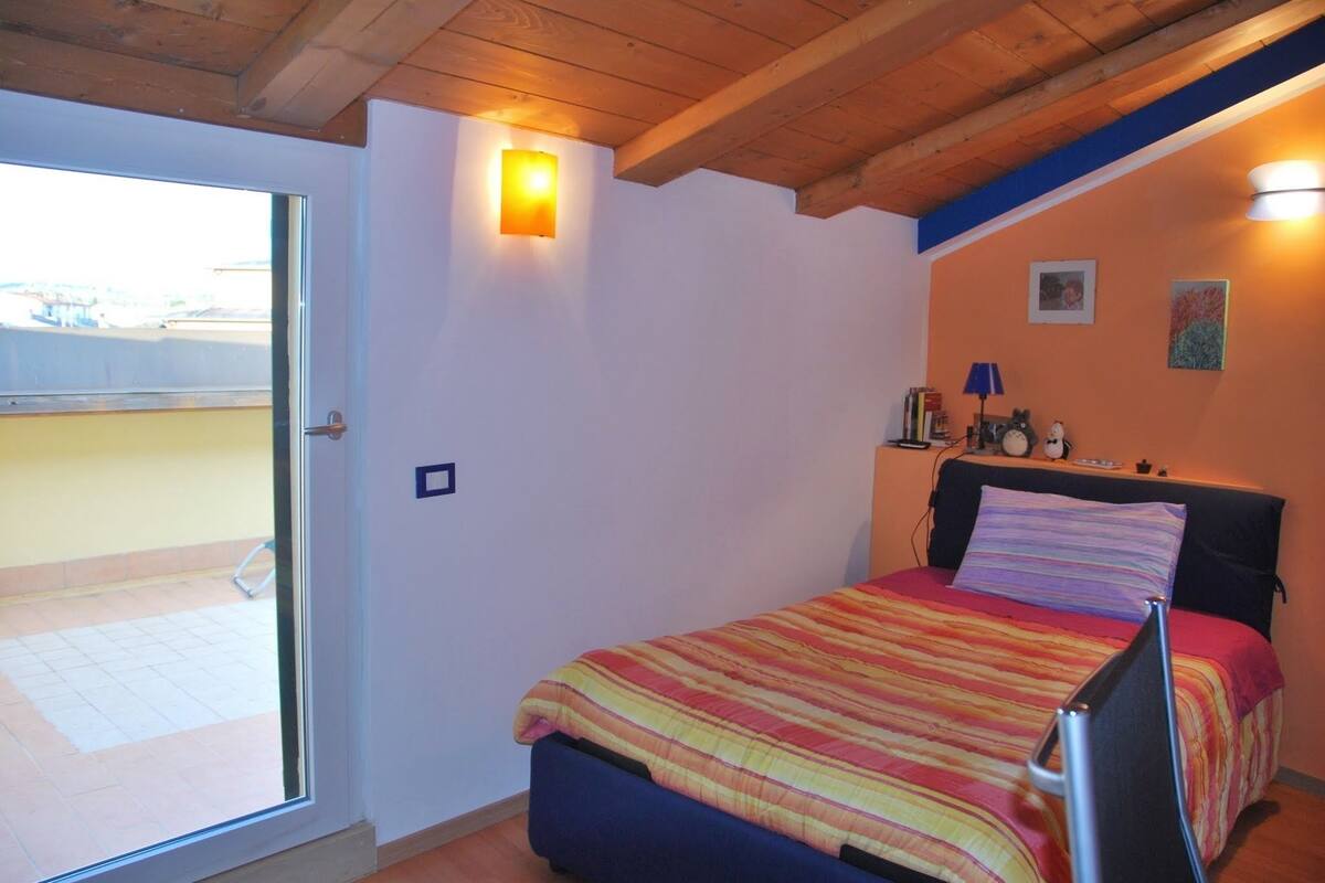 A bedroom with a bed, a window, a door, and a wall-mounted light fixture.