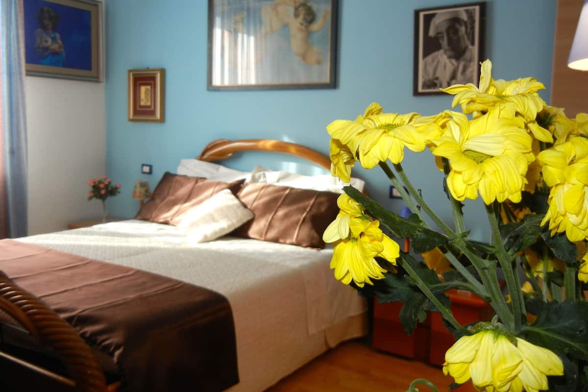A bedroom with a bed, pillows, and a vase of yellow flowers.