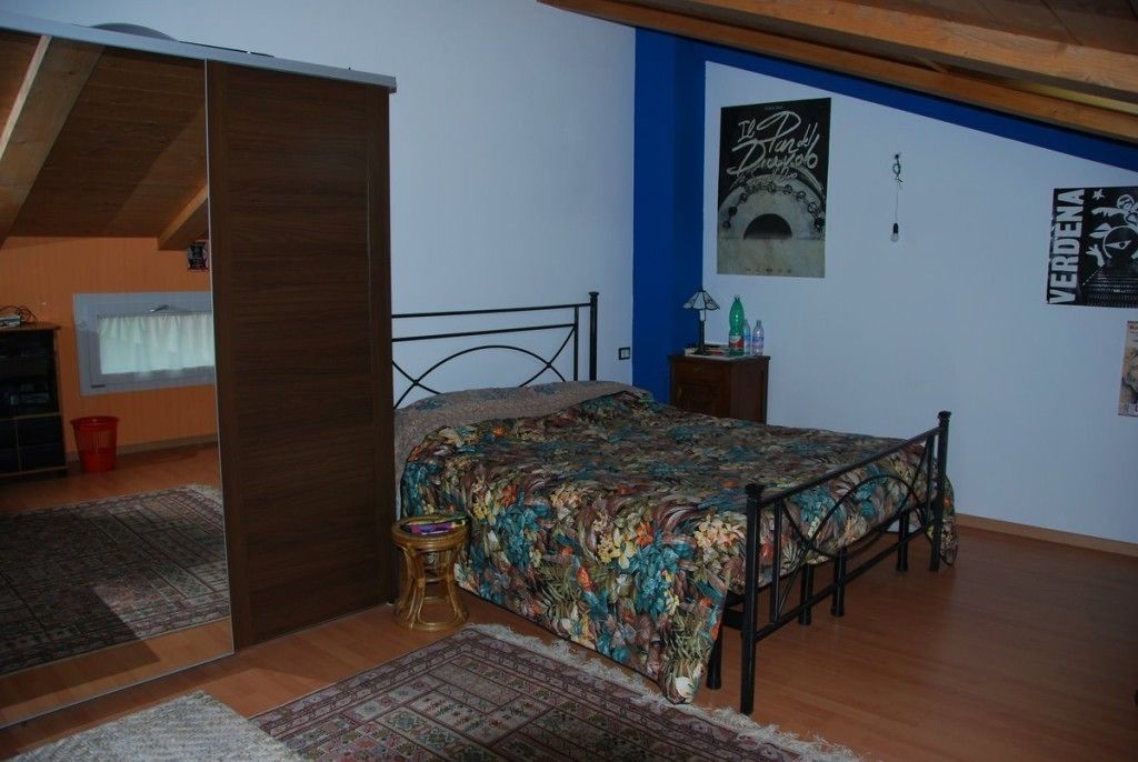 A bedroom with a bed, a small stool, a nightstand, and a poster on the wall.
