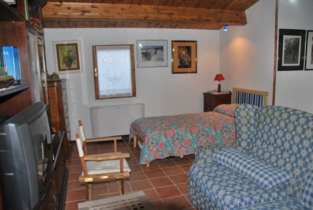 Une pièce comprenant un lit, un canapé, une chaise en bois, un téléviseur et des tableaux encadrés accrochés au mur.