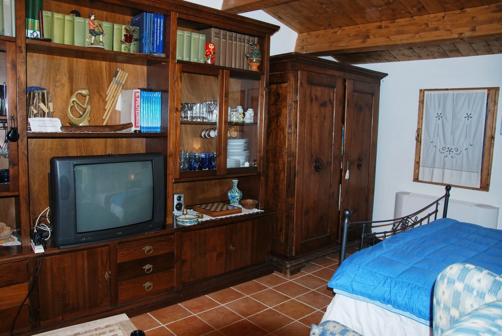 A room with a wooden cabinet containing books, a television, and various decorative items.
