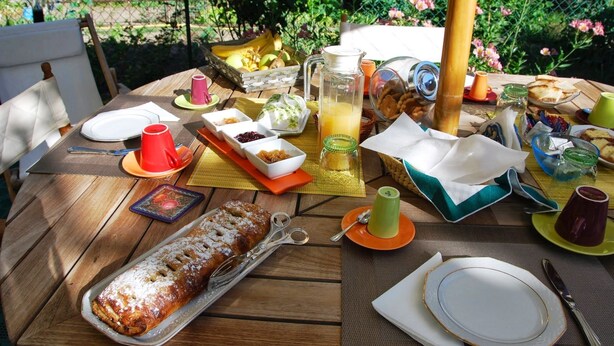 Una mesa de madera dispuesta con diversos alimentos, como una hogaza de pan, una jarra de jugo y varias tazas y platos.