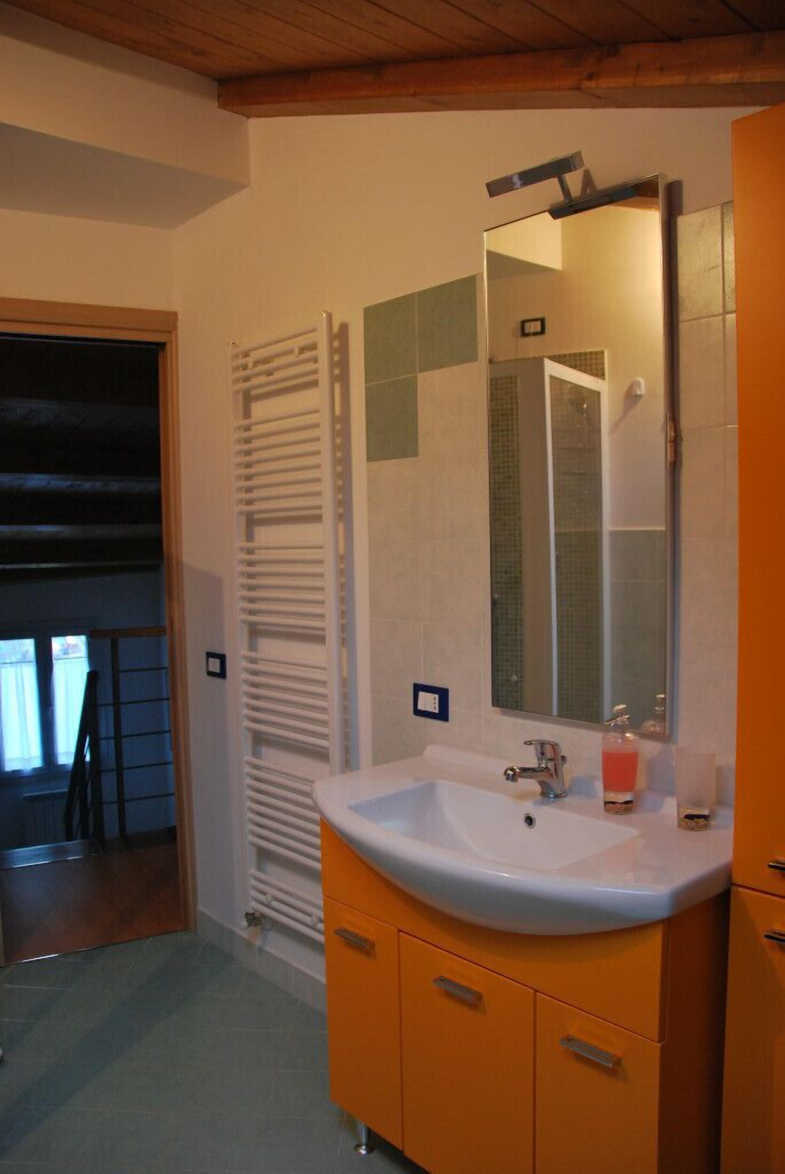 Un baño con un lavamanos blanco, armarios color naranja, un espejo y un perchero para toallas.