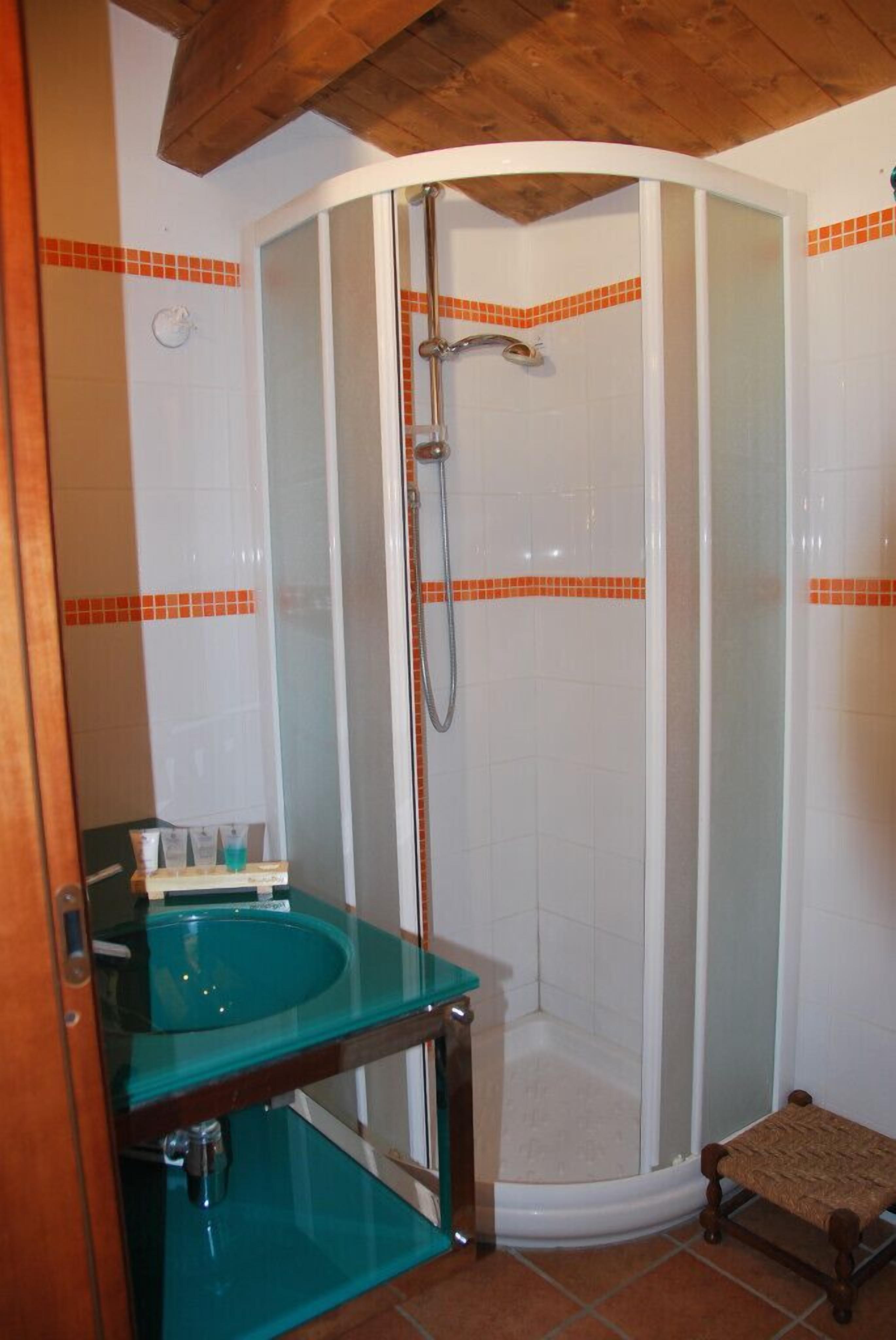 A corner shower with a glass enclosure and a wooden bench.