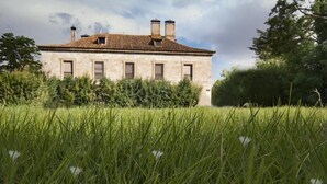 A stone building with a tiled roof, surrounded by tall grass and trees. - La Posada de Pradorey (Gumiel de Mercado)