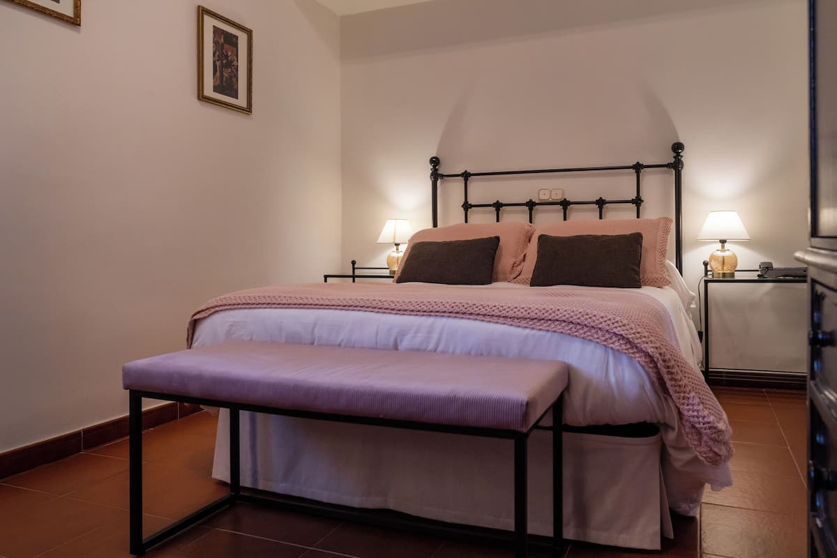 A bedroom with a bed, bedside tables, a bench, and a wall-mounted picture.