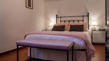 Un dormitorio con cama, mesitas de noche, un banco y un cuadro en la pared.