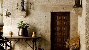 A rustic stone wall with a wooden door, a table with a potted plant, a brass bell, and a small statue. - La Posada de Pradorey (Gumiel de Mercado)