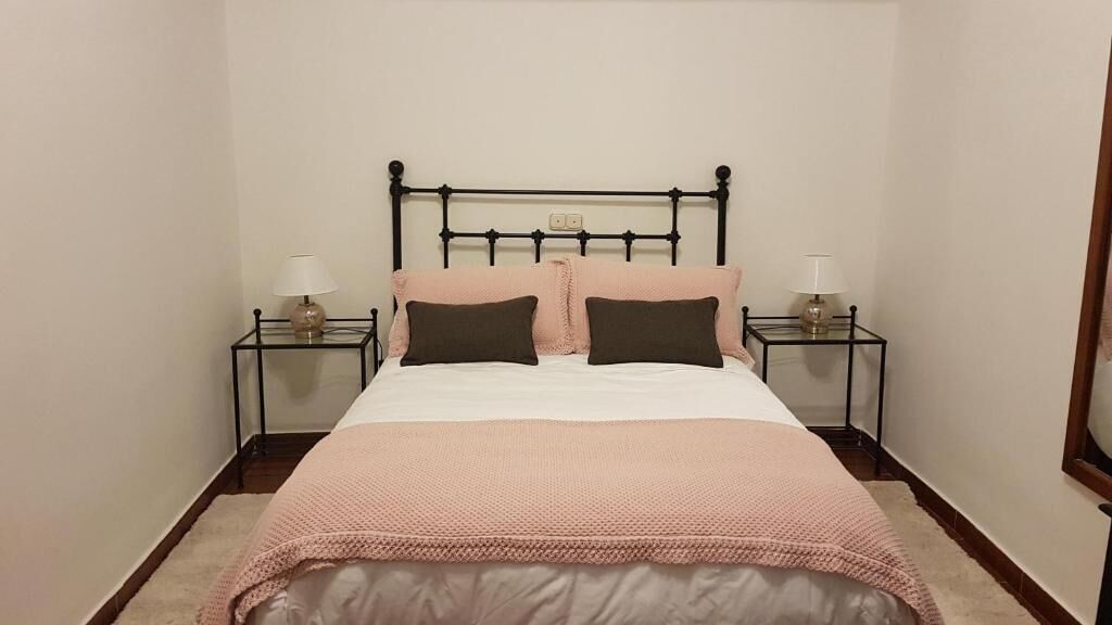 A neatly made bed with a pink blanket and two pillows, flanked by two bedside tables with lamps.