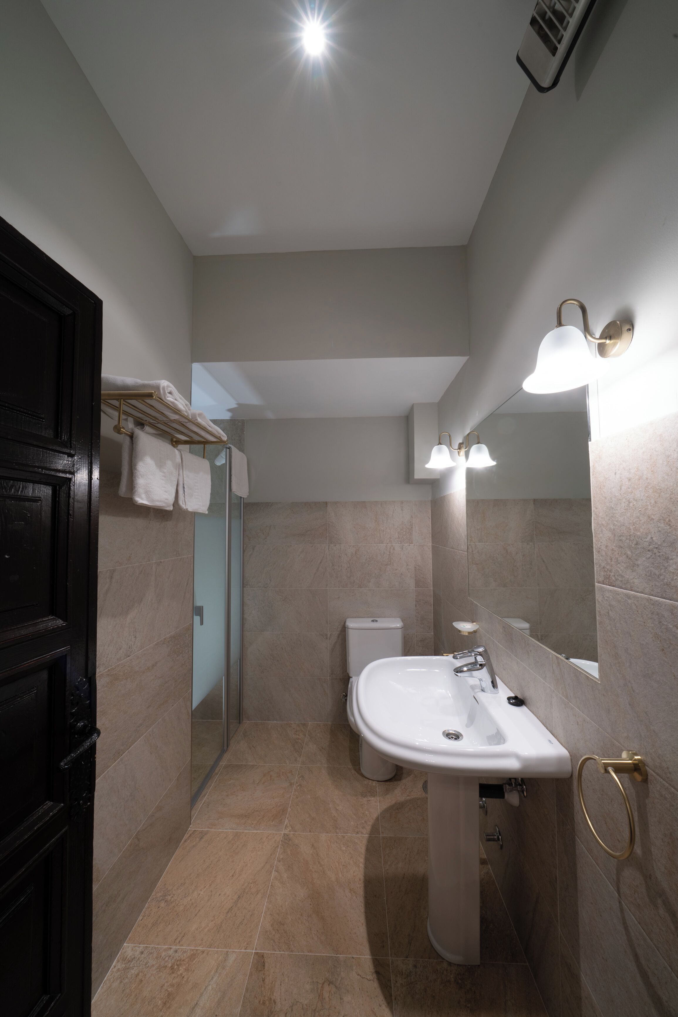 Un baño moderno con cabina de ducha de vidrio, un lavamanos blanco y un espejo grande con luces empotradas.