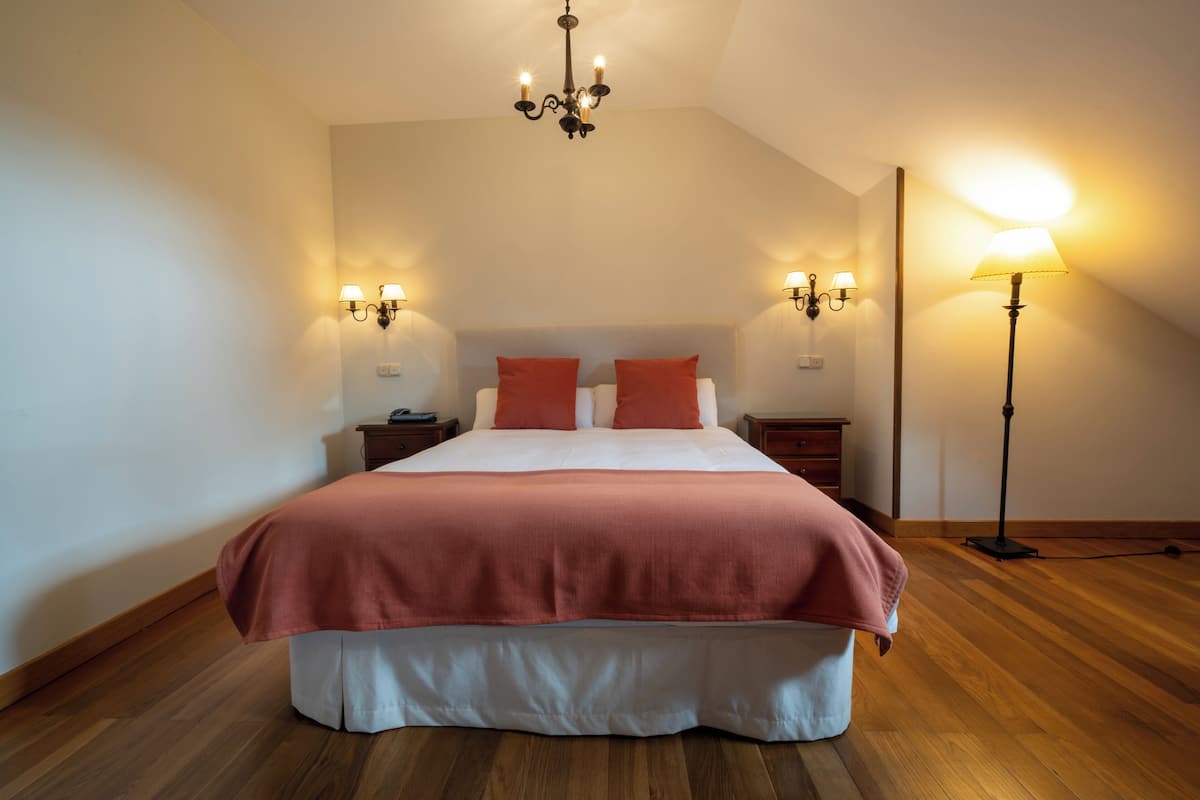 A bedroom with a large bed, two bedside tables, a floor lamp, and a chandelier.