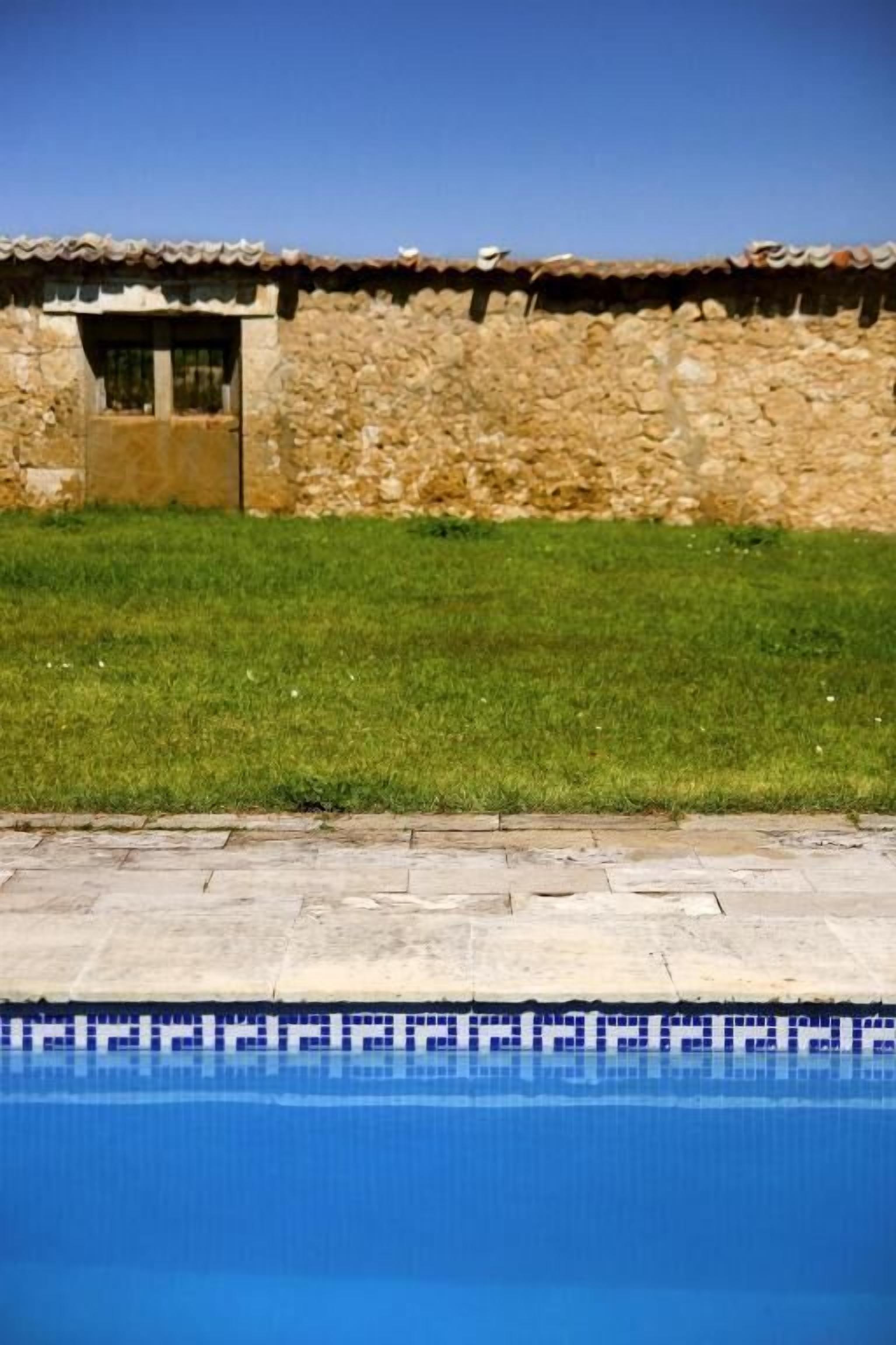A stone building with a tiled roof, a grassy area, and a swimming pool.