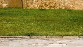 A stone building with a tiled roof, a grassy area, and a swimming pool.