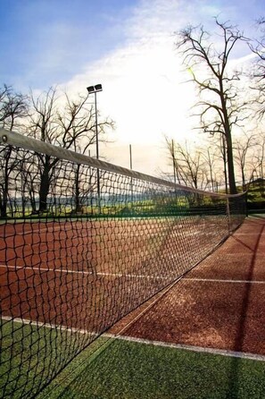 Una cancha de tenis con red, rodeada de árboles y un cielo despejado.