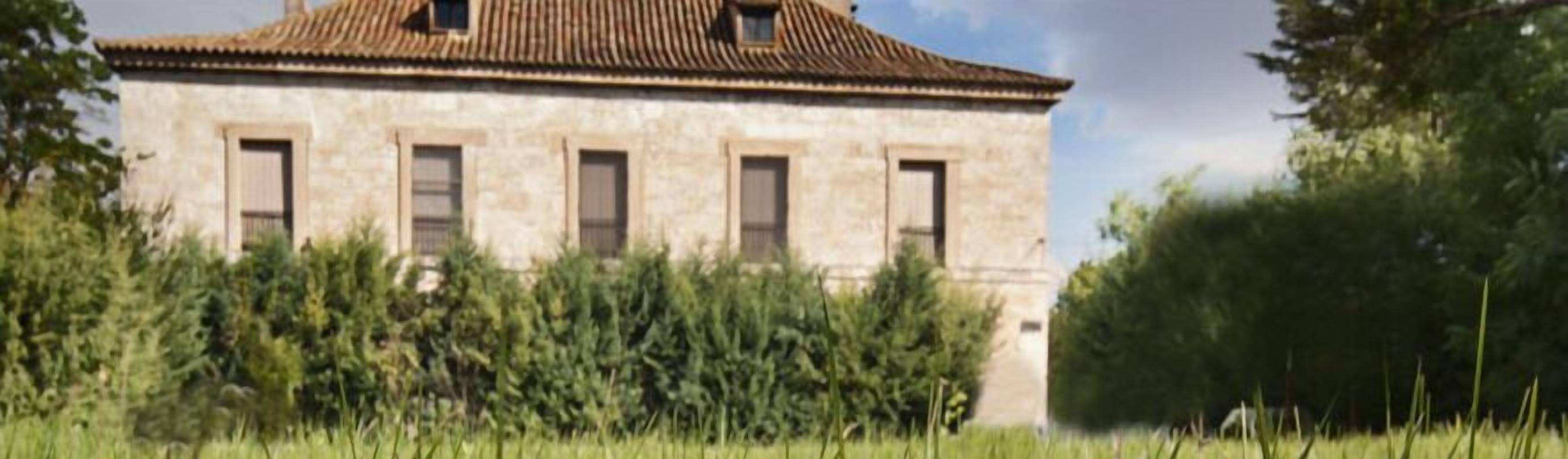 A stone building with a tiled roof, surrounded by greenery.