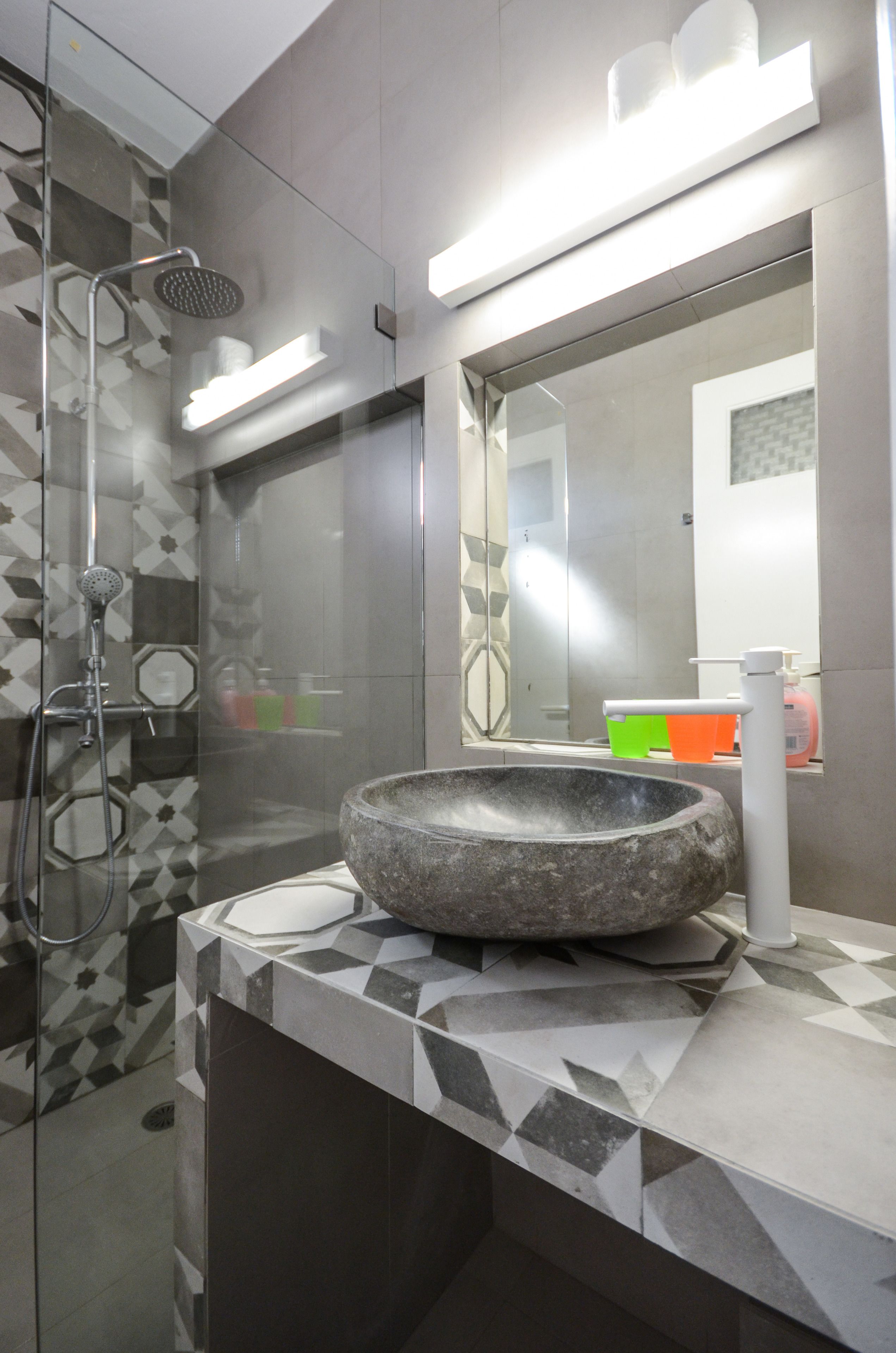 A modern bathroom with a glass-enclosed shower, a large mirror, and a stone basin sink.