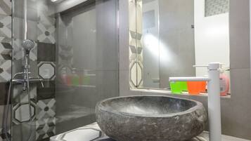 A modern bathroom with a glass-enclosed shower, a large mirror, and a stone basin sink.
