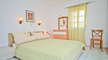 Un dormitorio con cama, lámparas de noche, cómoda de madera, una silla y una ventana con cortinas.