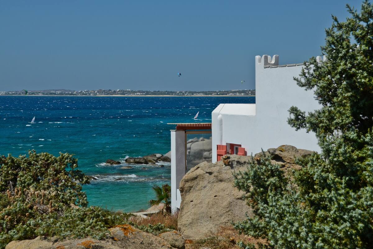 Blick auf die Küste mit einem weißen Gebäude, felsigem Gelände und dem Meer.