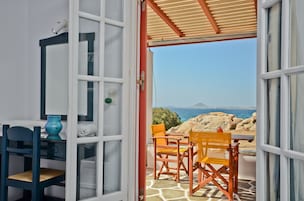 Una habitación con vistas al mar, una mesa con sillas y una ventana que da a terreno rocoso.