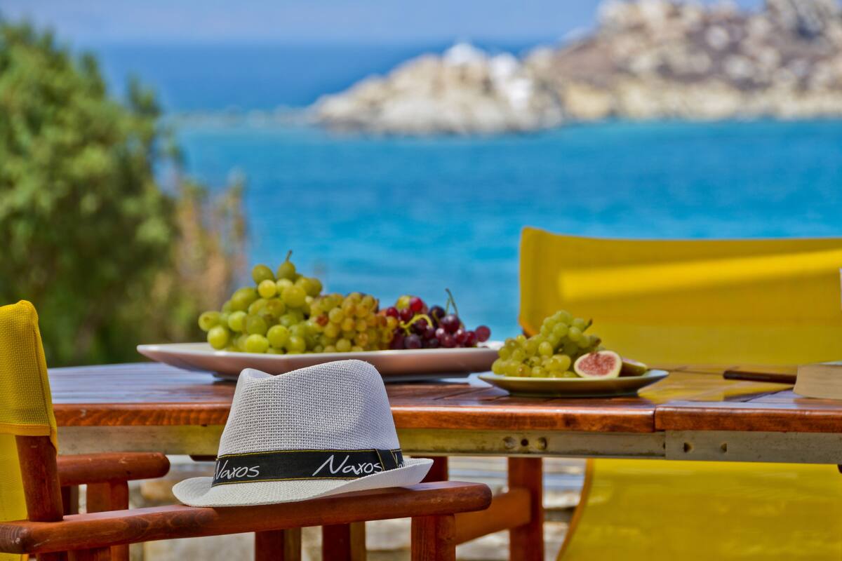 Ein Tisch mit einem Hut, Teller mit Trauben und Blick auf das Meer.