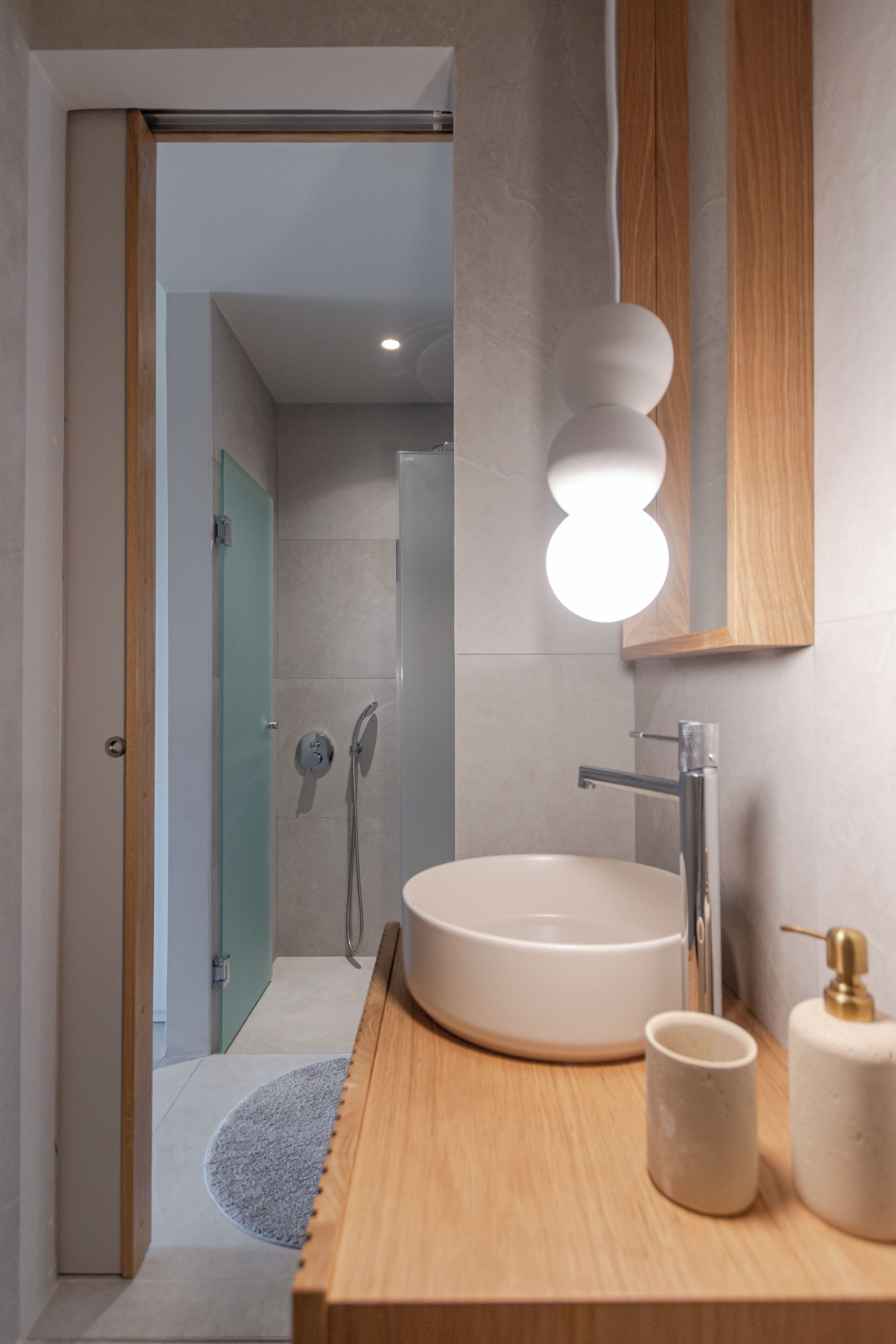 Un baño moderno con un lavabo redondo, un espejo con marco de madera y una zona de ducha visible al fondo.