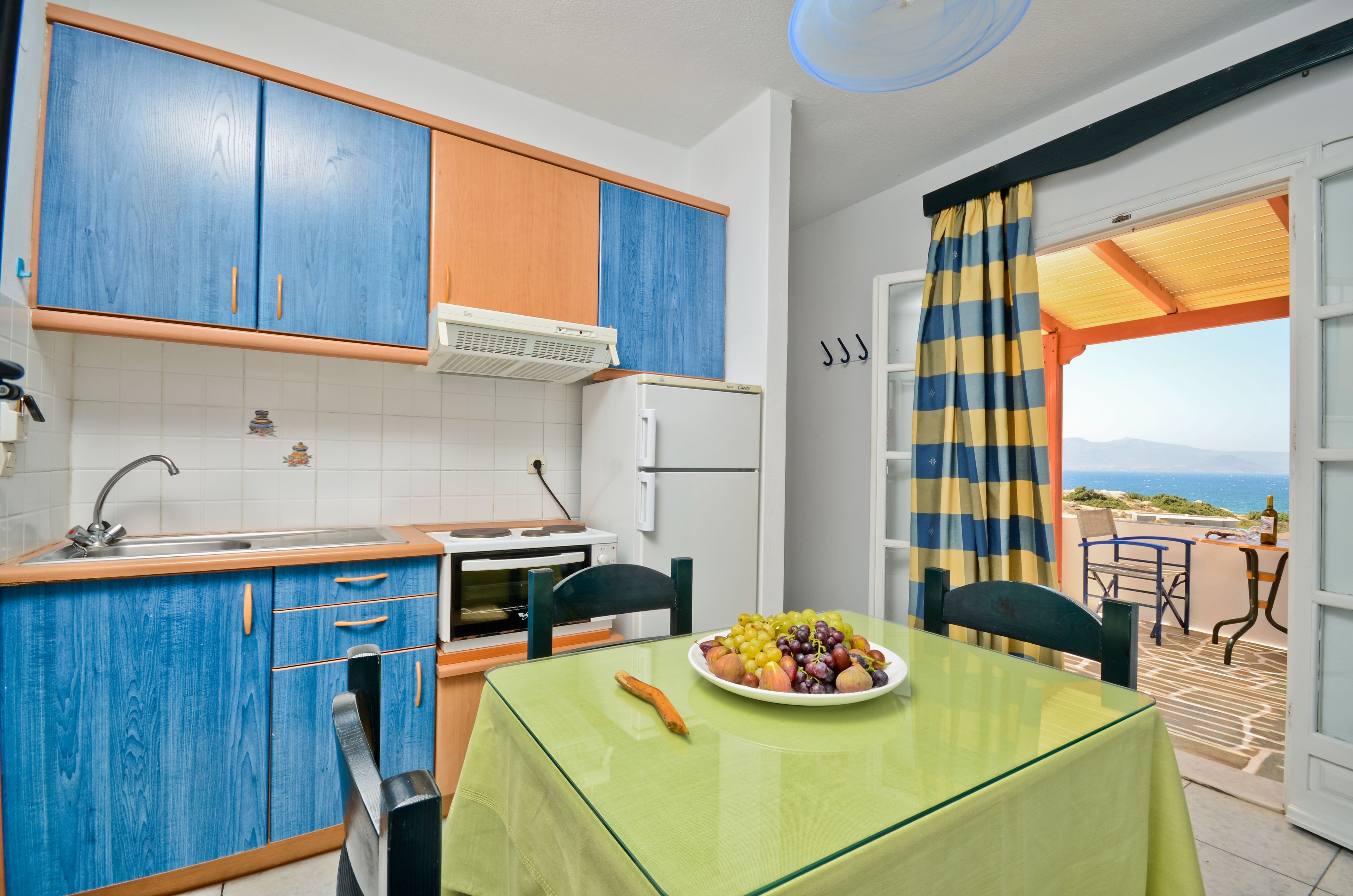 Una cocina con armarios azules, un refrigerador blanco y una mesa de comedor con una fuente de frutas.