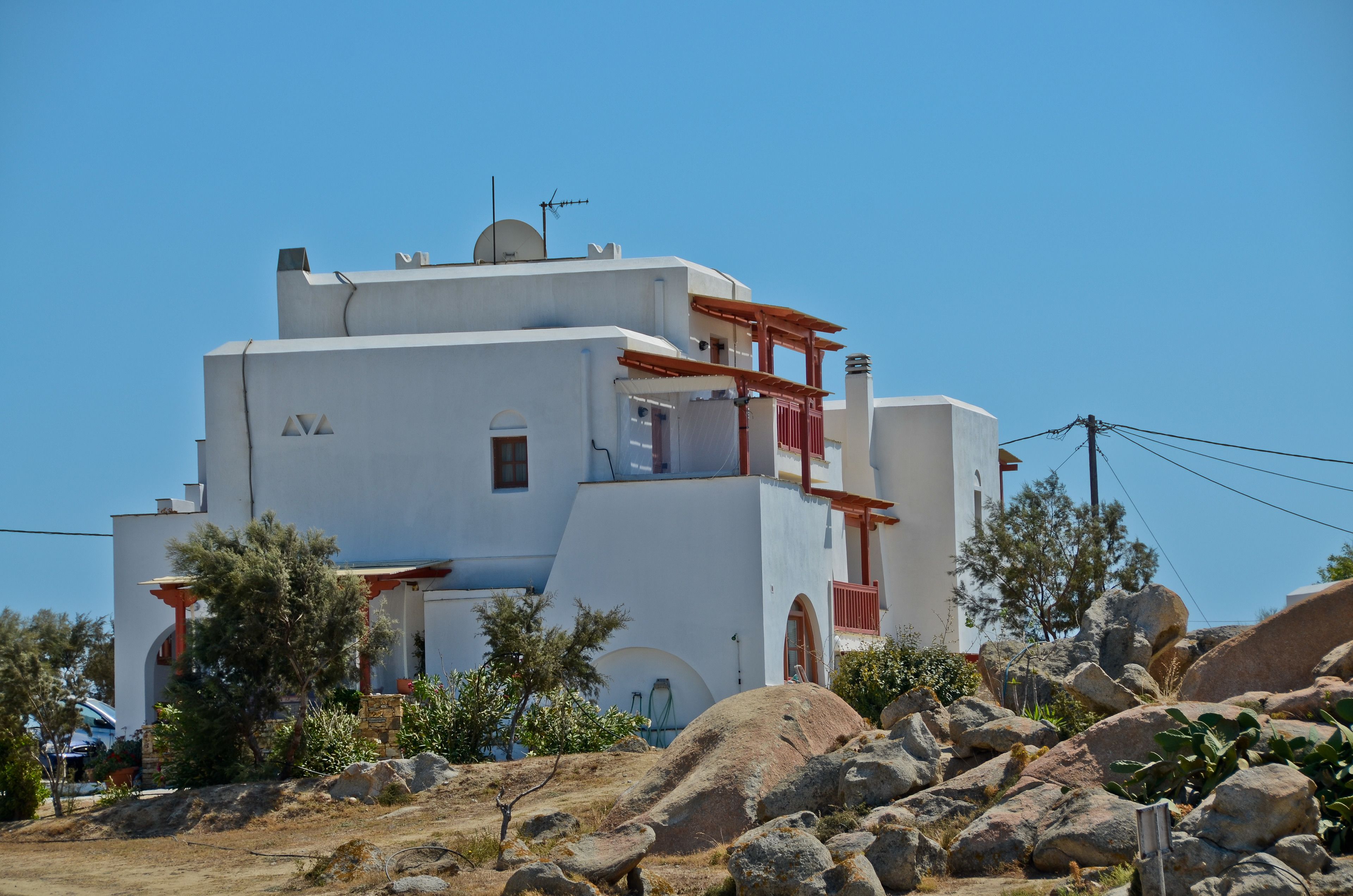 Un bâtiment blanc doté d’un balcon rouge, entouré de rochers et d’une végétation clairsemée.