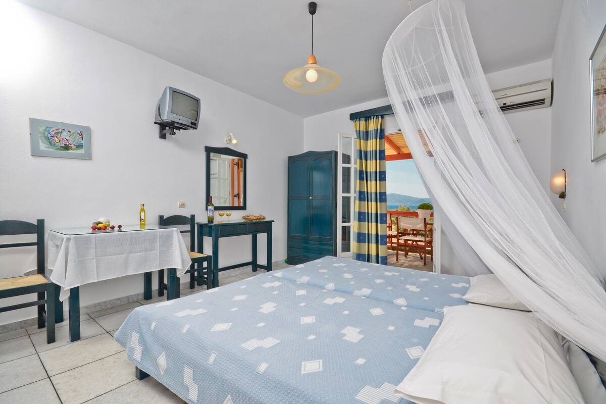 Ein Schlafzimmer mit Bett, Schreibtisch, Stuhl, Tisch, Fernseher und einem Fenster mit Vorhängen.