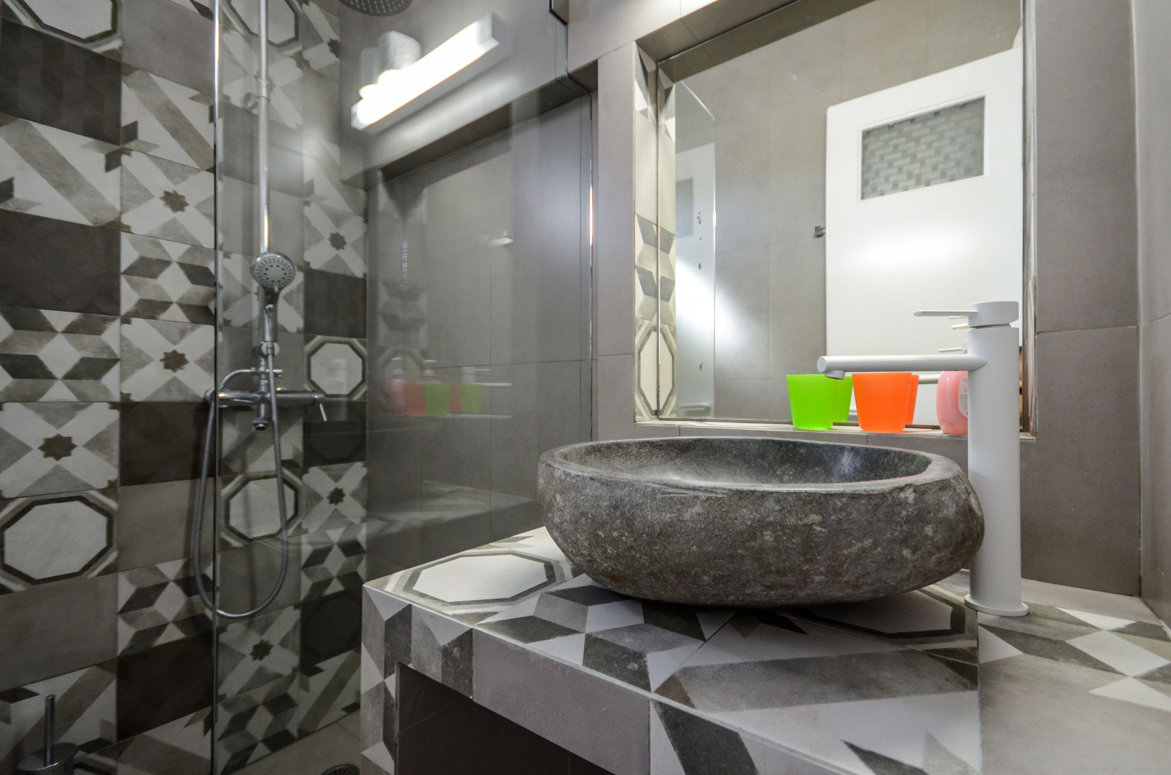 A modern bathroom with a stone basin sink, a glass shower enclosure, and a geometric tile backsplash.