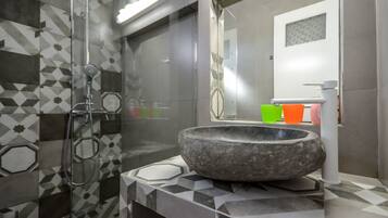 A modern bathroom with a stone basin sink, a glass shower enclosure, and a geometric tile backsplash.