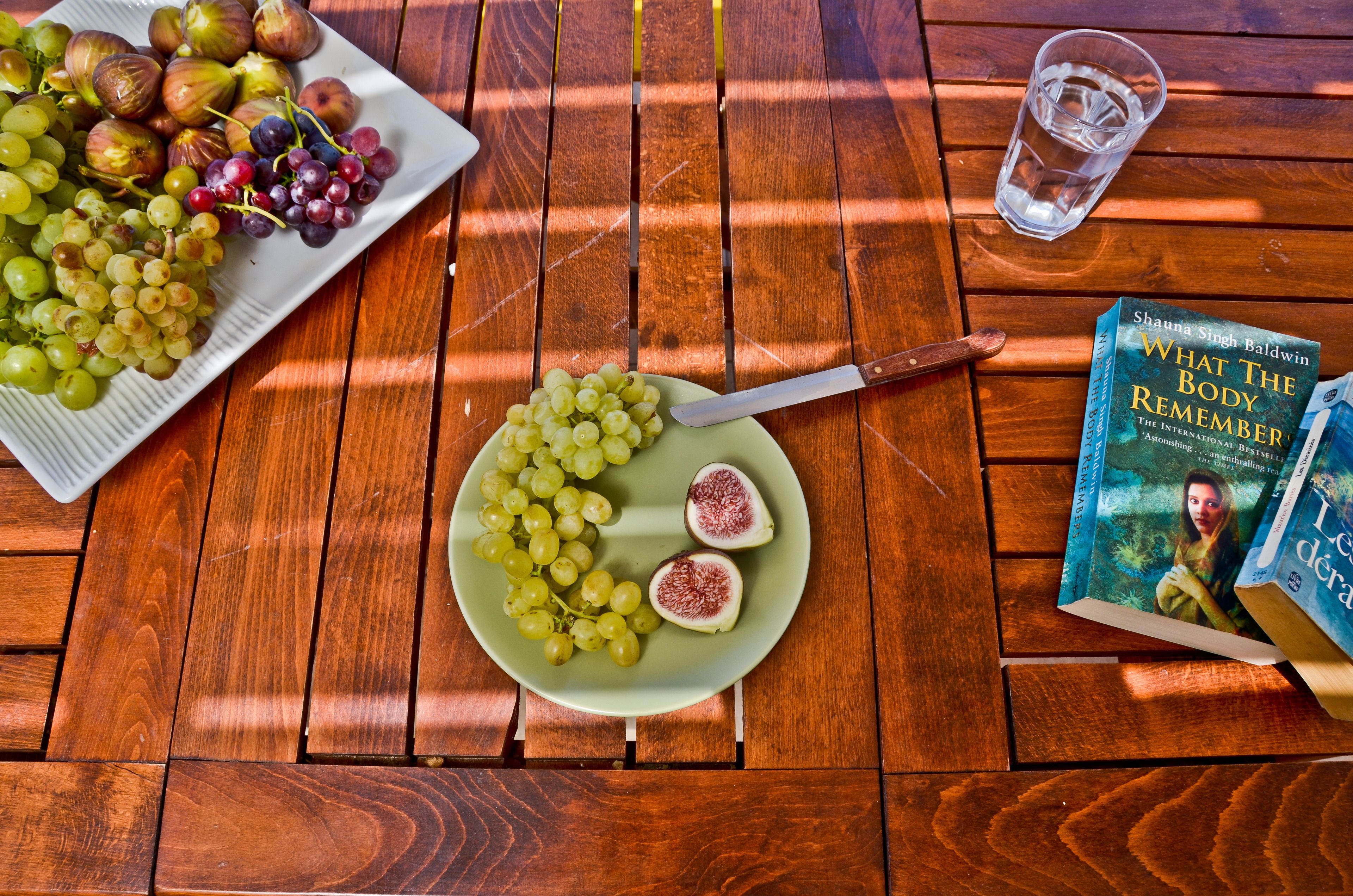A wooden table with a plate of grapes and figs, a glass of water, and a book titled "What the Body Remembered".