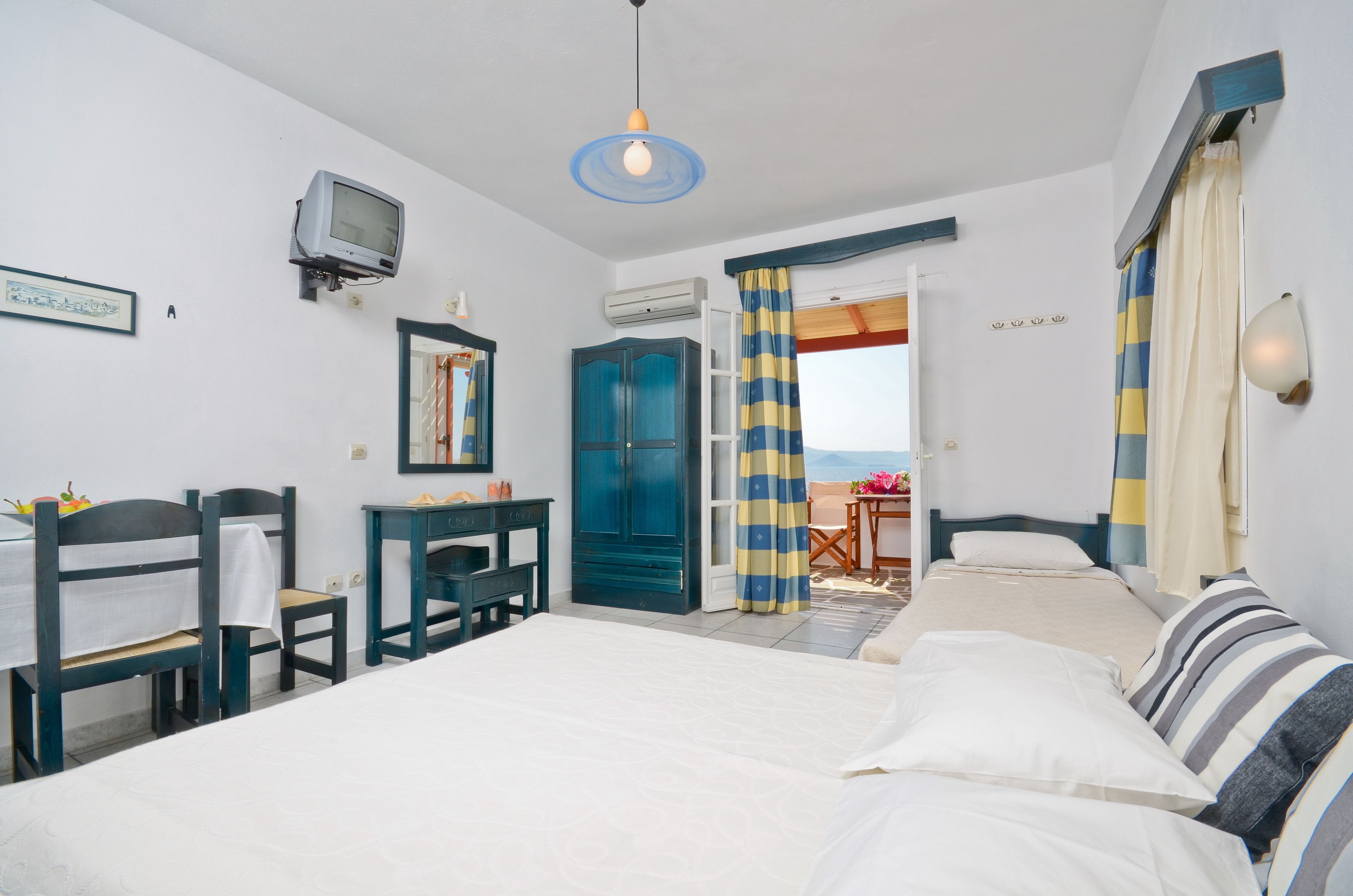 Un dormitorio con cama, escritorio, silla, televisor y vista a la playa.