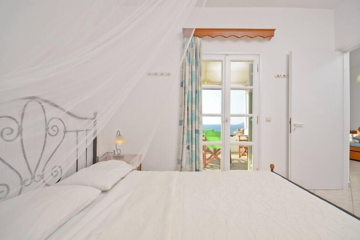 Ein Schlafzimmer mit einem Bett, einem Nachttisch, einem Fenster mit Vorhängen und einer Tür, die auf einen Balkon führt.