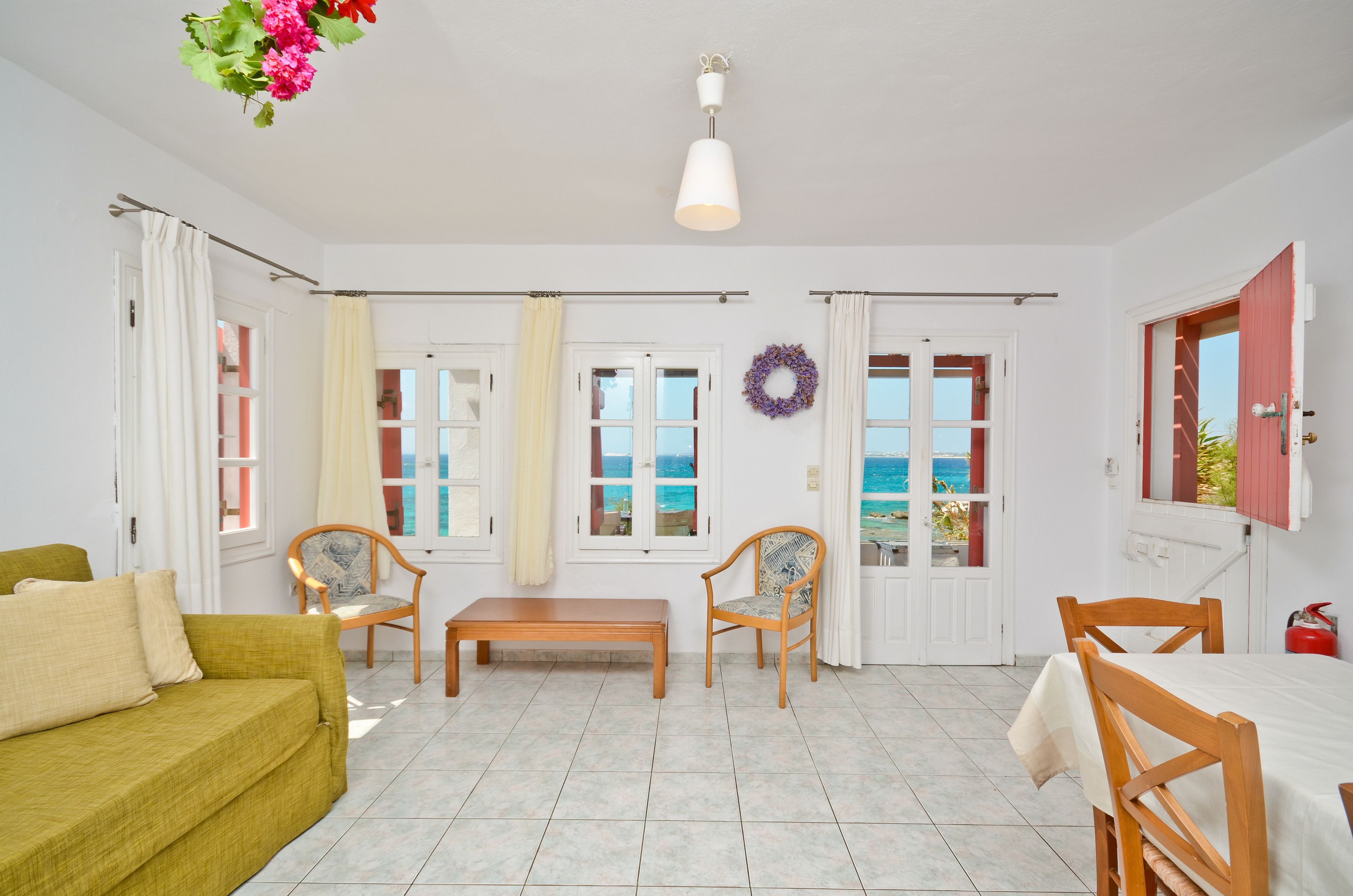 Una habitación luminosa con sofá, sillas, una mesa y vistas al mar a través de ventanas.
