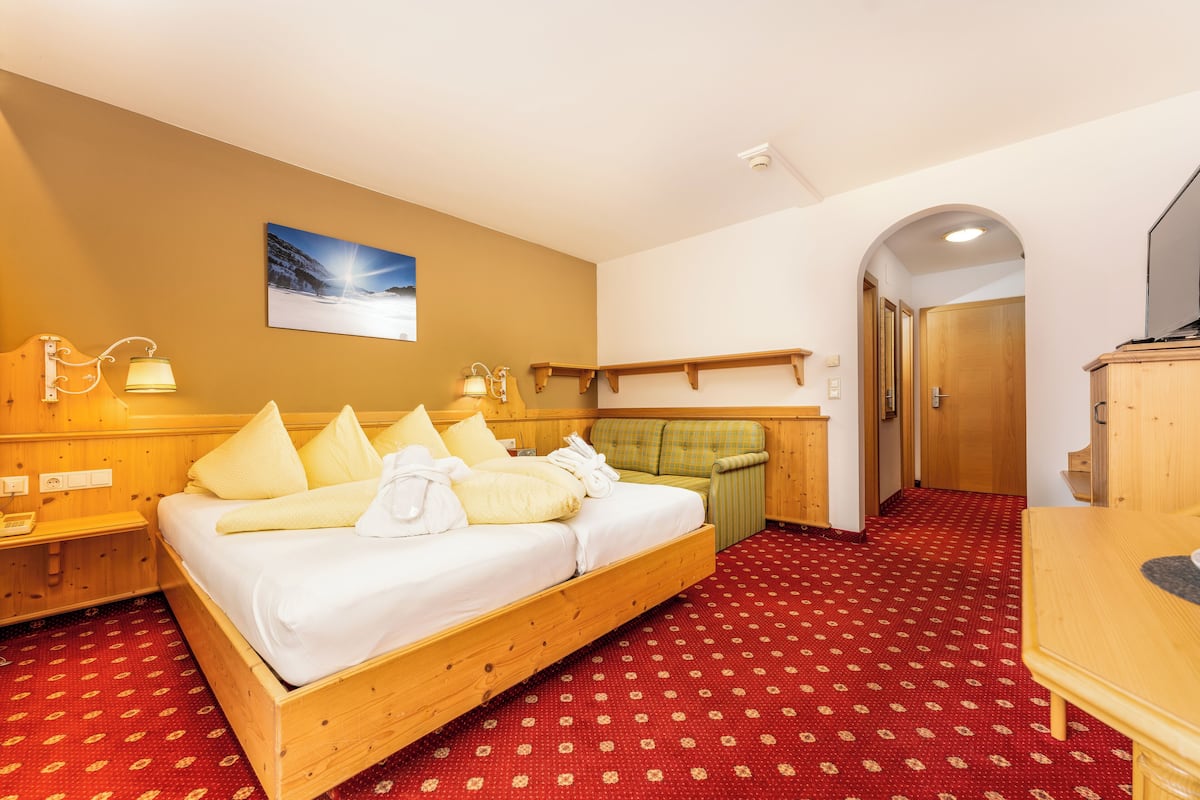Ein Hotelzimmer mit einem hölzernen Bett, einem roten Teppich mit Muster, einem Bild an der Wand und einem Holz-Kopfstück.