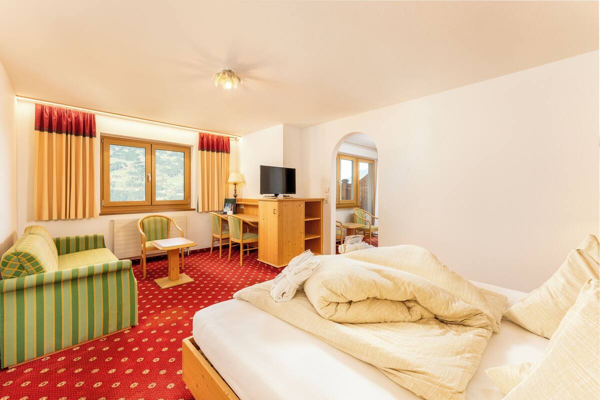 Ein Hotelzimmer mit Bett, einer Sitzecke, einem Schreibtisch mit Stuhl, einem Fernseher und einem Fenster mit Vorhängen.