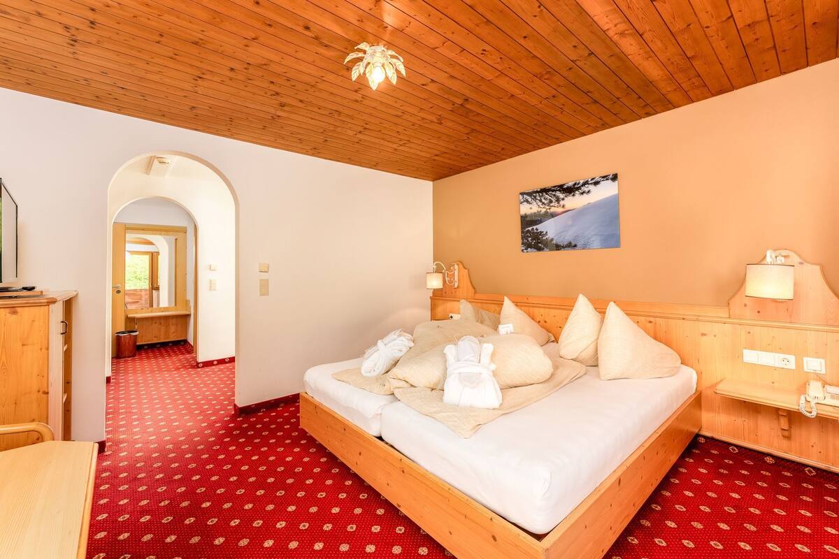 Ein Bett mit Holzrahmen, Handtücher, ein Holz-Kopfteil und ein roter Teppich mit Muster.