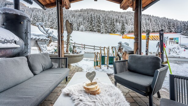 A covered outdoor seating area with a sofa and chairs, a heart-shaped decoration, and a view of a snowy landscape.