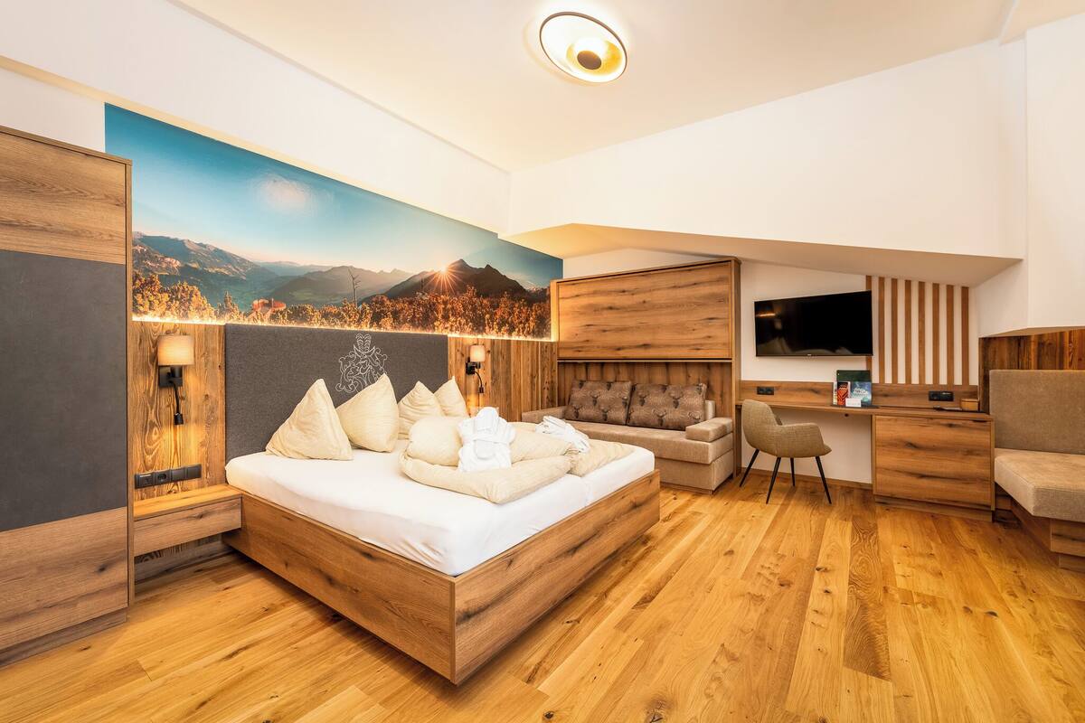 Ein modernes Schlafzimmer mit einem hölzernen Bett, einem Schreibtisch, einem Fernseher und einem großen Fenster mit Bergblick.