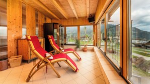 A wooden interior with two red lounge chairs, a television, and large windows offering a view of the outdoors.