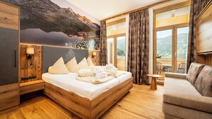 A modern bedroom with a wooden bed, a sofa, a small table, and a large window with curtains.