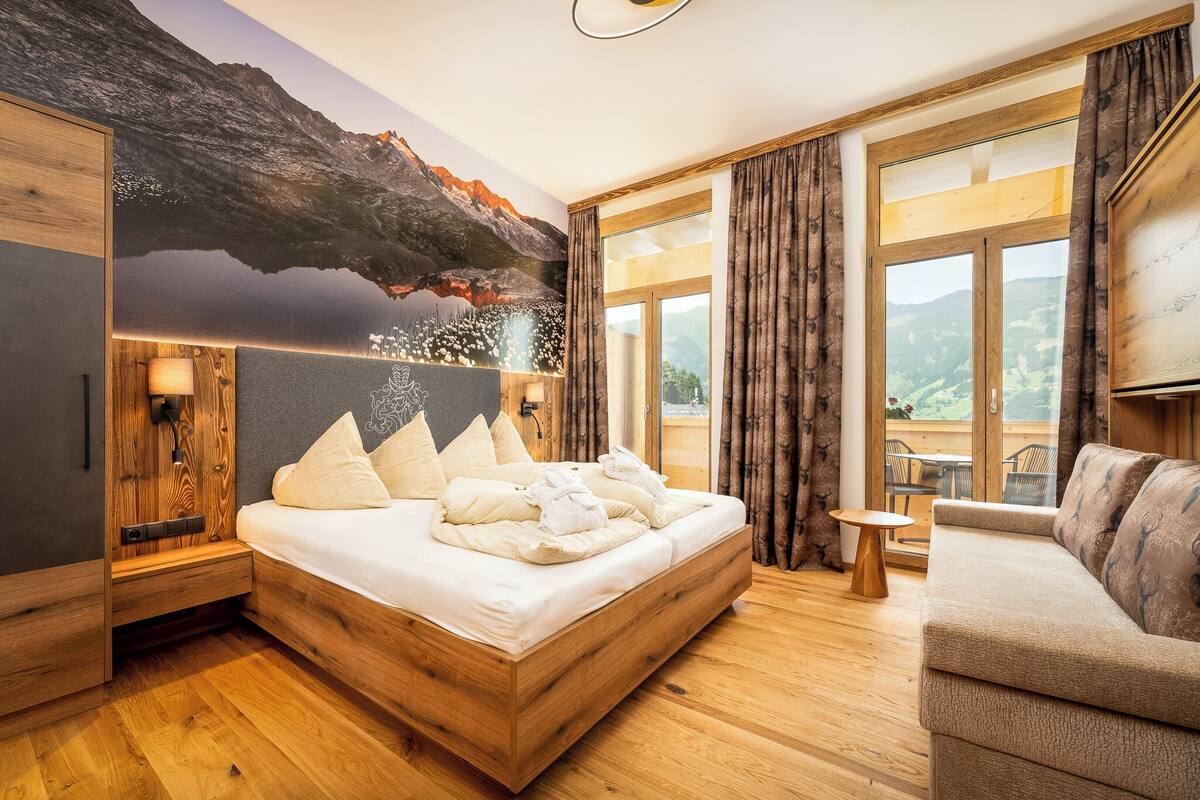 Ein modernes Schlafzimmer mit einem hölzernen Bett, einer Couch, einem kleinen Tisch und einem gro ßen Fenster mit Vorhängen.