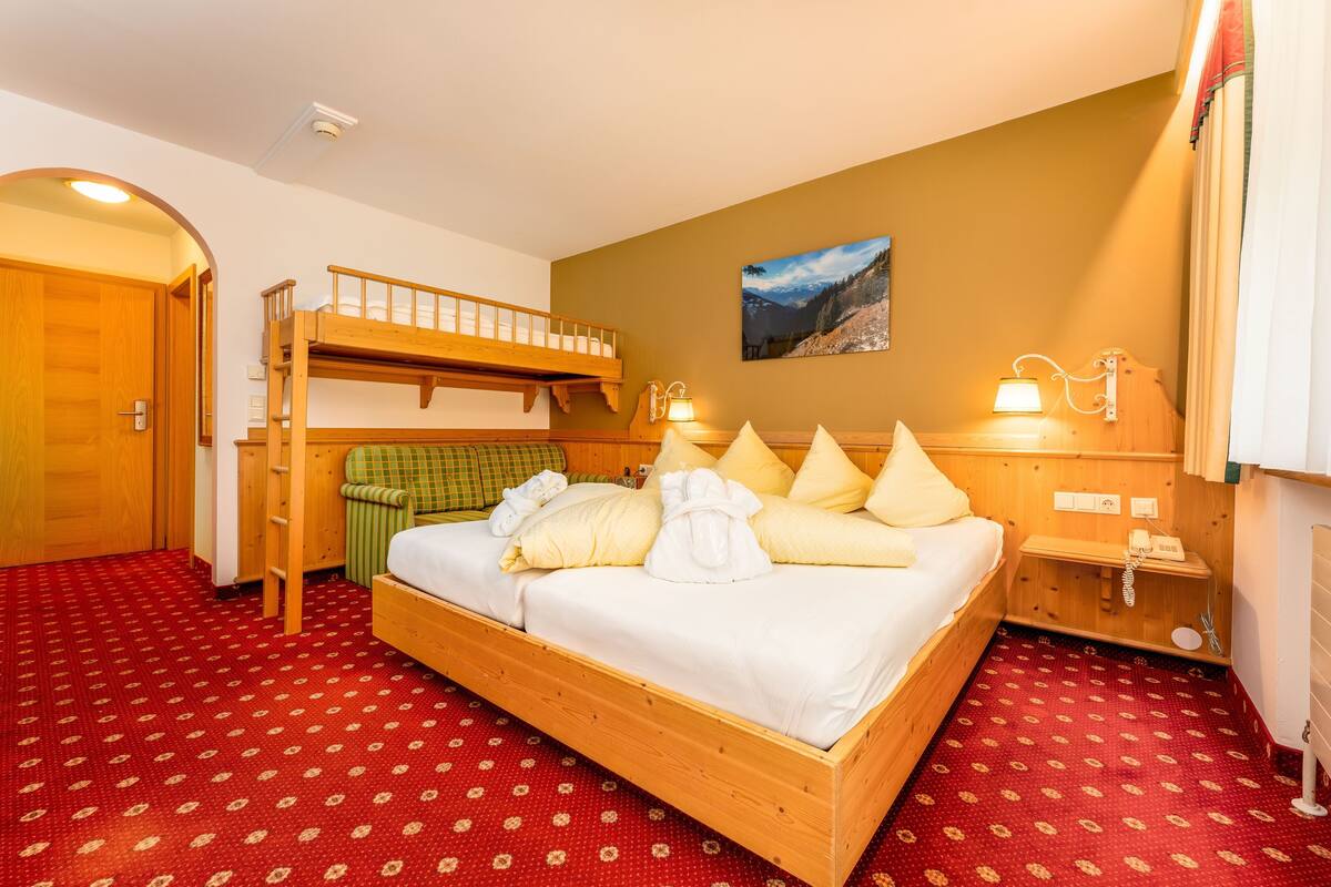 Ein Zimmer mit einem Etagenbett, einem Einzelbett, einem roten Teppich mit Muster, einem Bild an der Wand und einem kleinen Nachttisch mit Lampe.