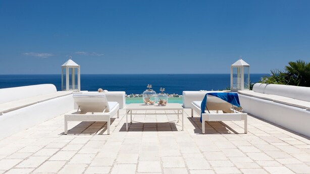 Une terrasse avec des meubles blancs, une table agrémentée d’objets décoratifs et une vue sur la mer.