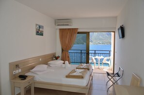 A hotel room with a bed, a bedside table with a phone, a window with curtains, a view of the sea, and a balcony with chairs. - Hotel Plaza (Kalymnos)