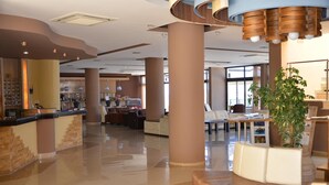 A spacious lobby with a reception desk, seating areas, and a large plant. - Hotel Plaza (Kalymnos)