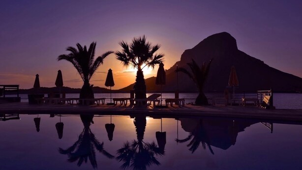 A serene sunset view with a pool reflecting palm trees and a mountain in the background. - Hotel Plaza (Kalymnos)